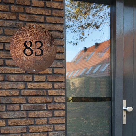 Rond naambordje voordeur roest aan donkere muur